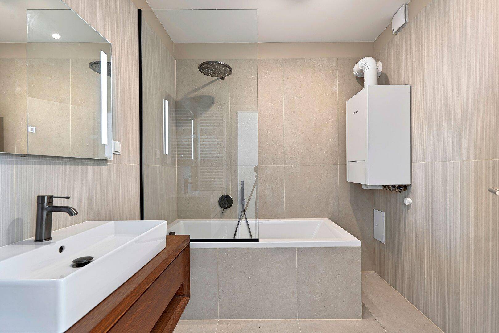 Modernes Badezimmer mit Badewanne, Regendusche, Einzelwaschbecken und beigefarbenen Fliesen.