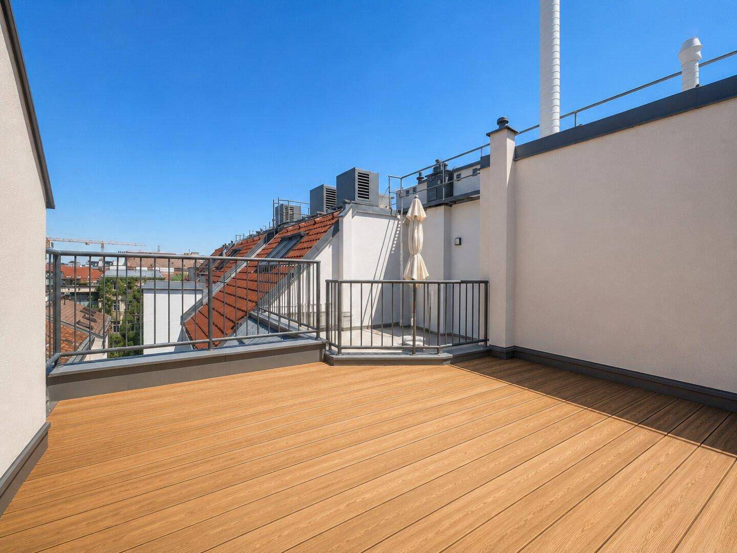 Weitläufige Dachterrasse mit Holzboden und Blick auf die umliegenden Dächer der Stadt.