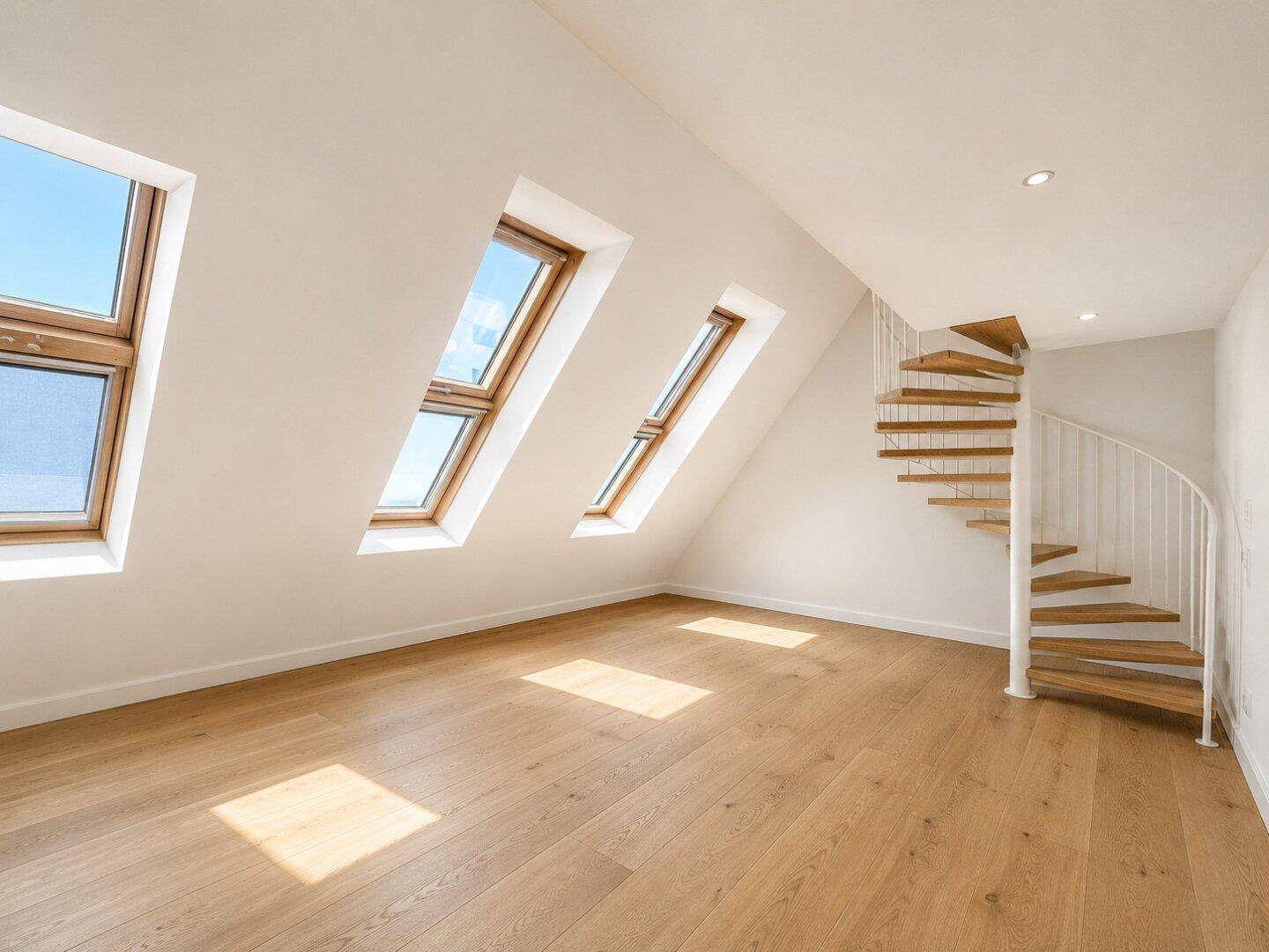 Heller Raum mit Holzboden, Dachschrägen und drei Dachfenstern, ergänzt durch eine Wendeltreppe.