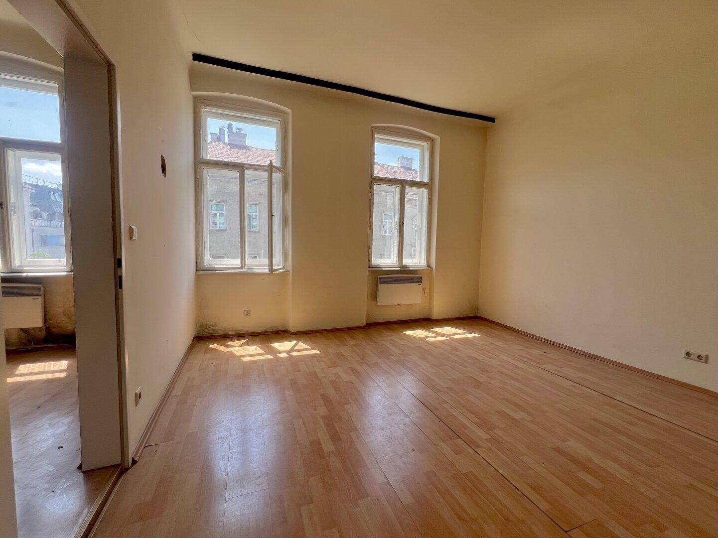 Geräumiges Zimmer mit Holzboden und viel Tageslicht durch die großen Fenster.