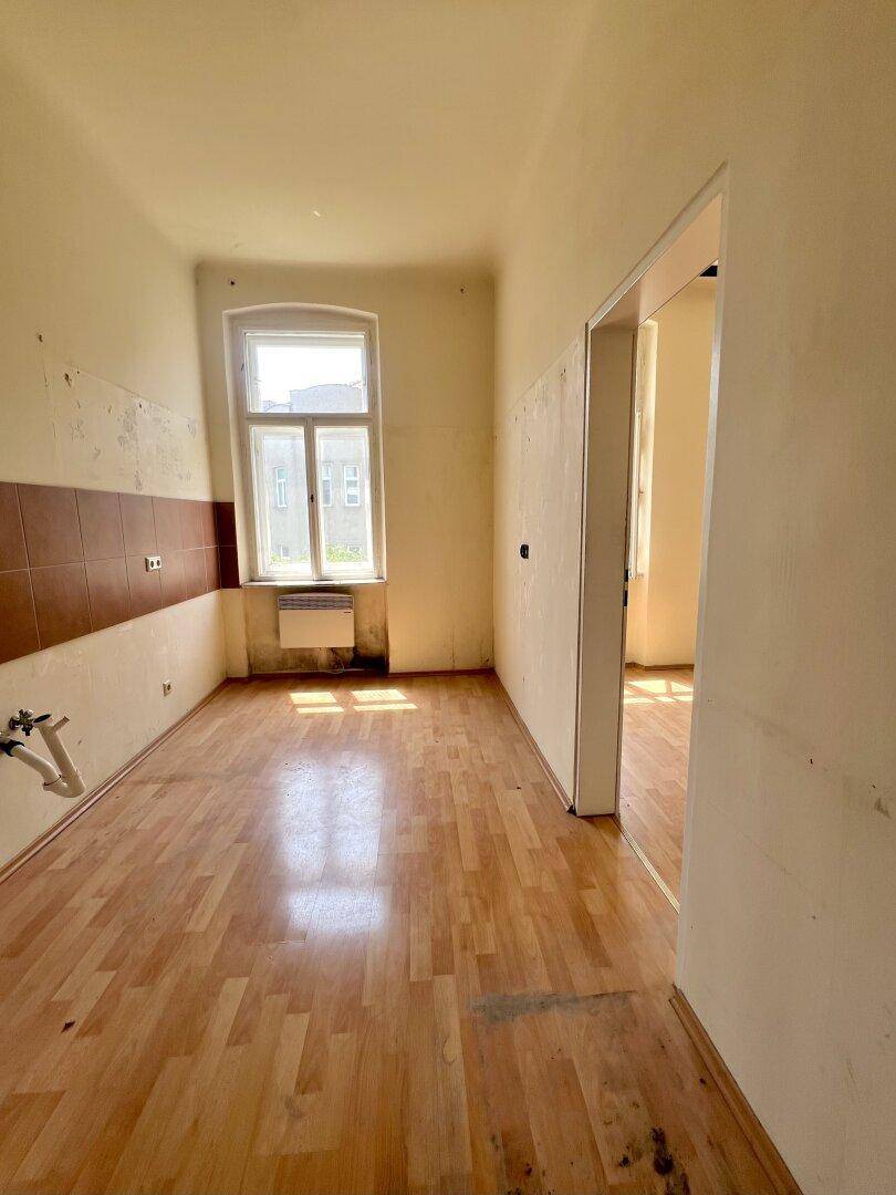 Leere Küche mit Parkettboden und gefliestem Wandbereich, bereit für neue Einbauten.