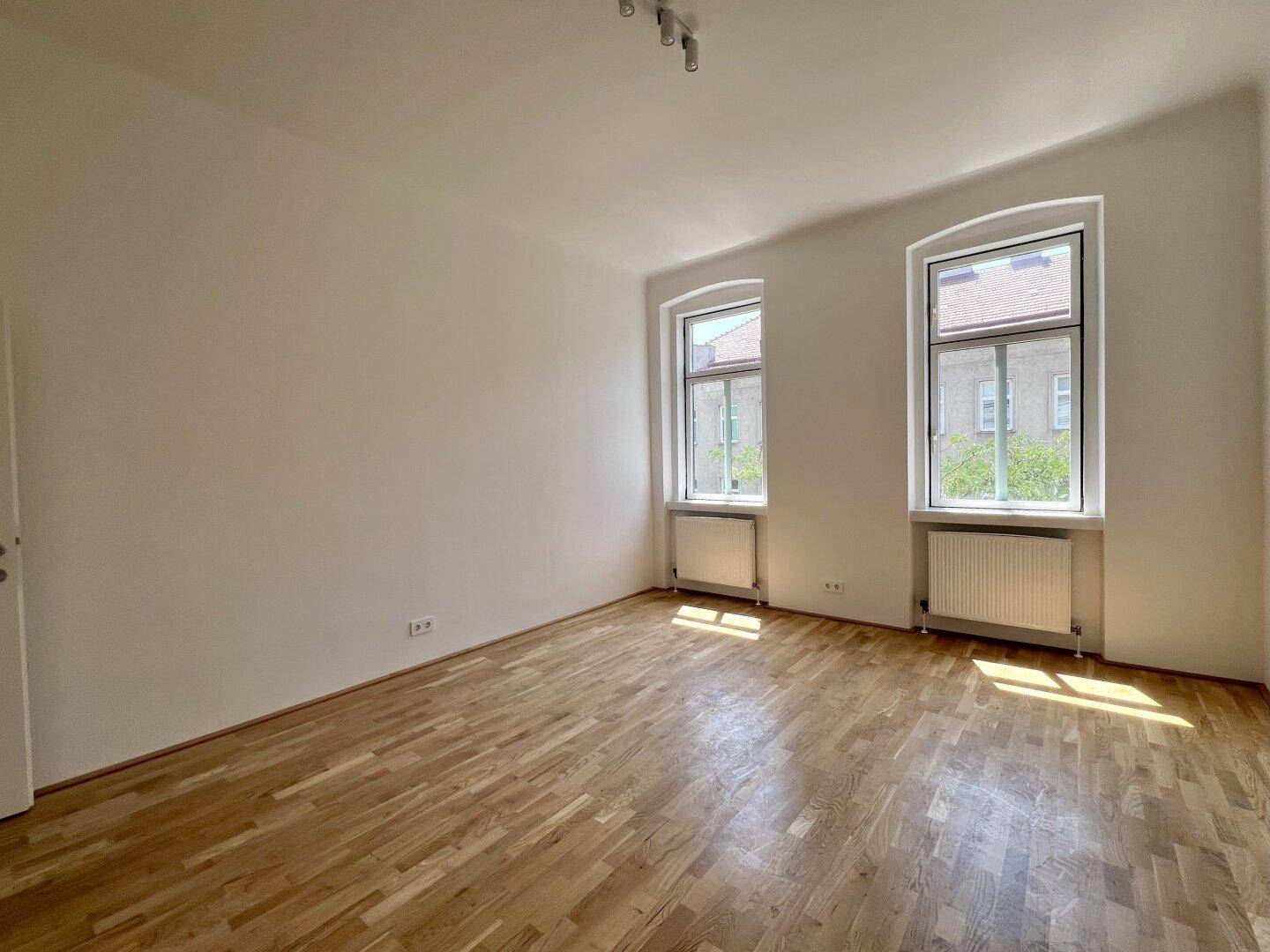 Geräumiges, helles Zimmer mit Parkettboden und großen Fenstern, bereit zur individuellen Gestaltung.