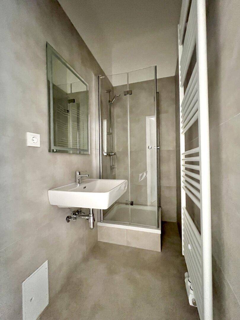 Modernes Badezimmer mit Duschkabine, Waschbecken und beheiztem Handtuchhalter in Grautönen.