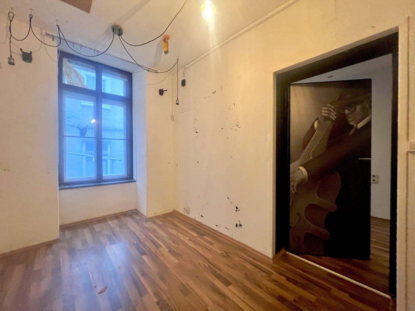 Leerer Raum mit Holzboden, einem Fenster und einer Tür mit einem Musikerbild.