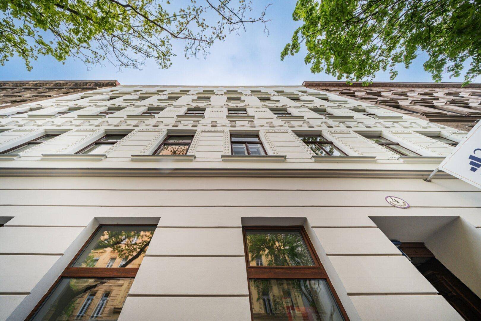 Ansicht der modernen Fassade eines Mehrfamilienhauses mit vielen Fenstern und Bäumen.
