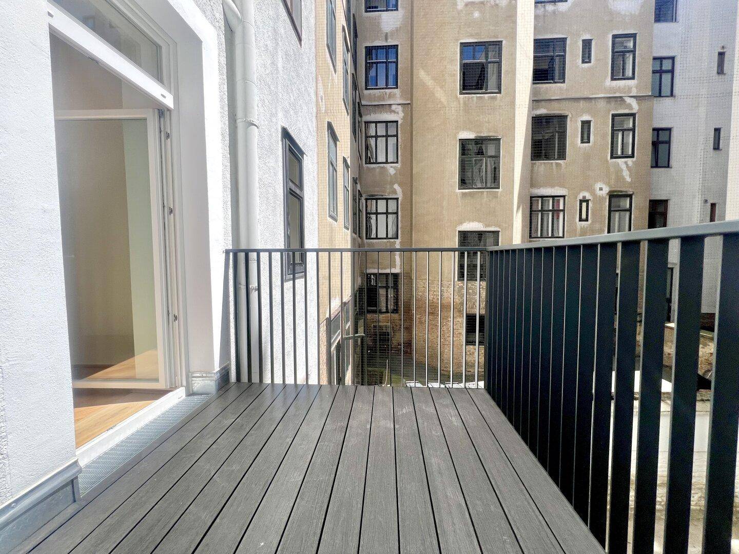 Balkon mit dunklem Bodenbelag und Blick auf den Innenhof, zugänglich vom Innenraum.