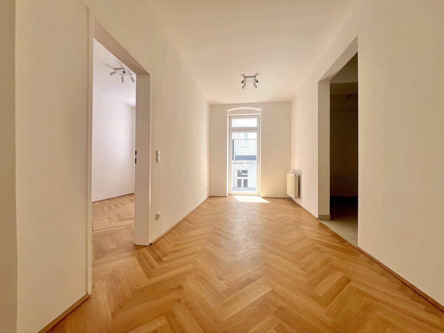 Langer Flur mit Fischgrätparkett, der zu weiteren Zimmern und einem hellen Fenster führt.