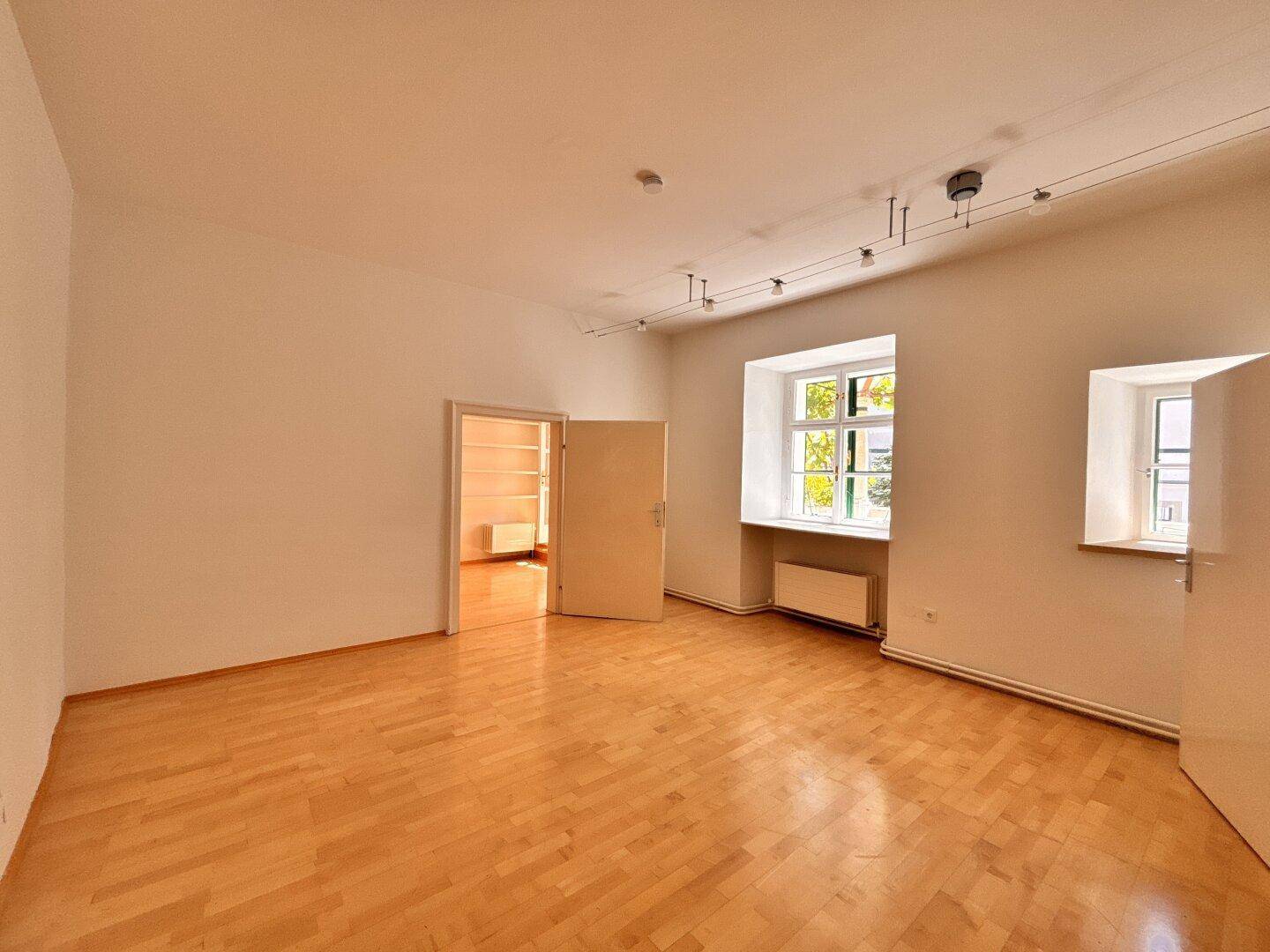 Heller, leerer Raum mit Holzboden, weißen Wänden und zwei Fenstern, ideal als Wohnbereich.