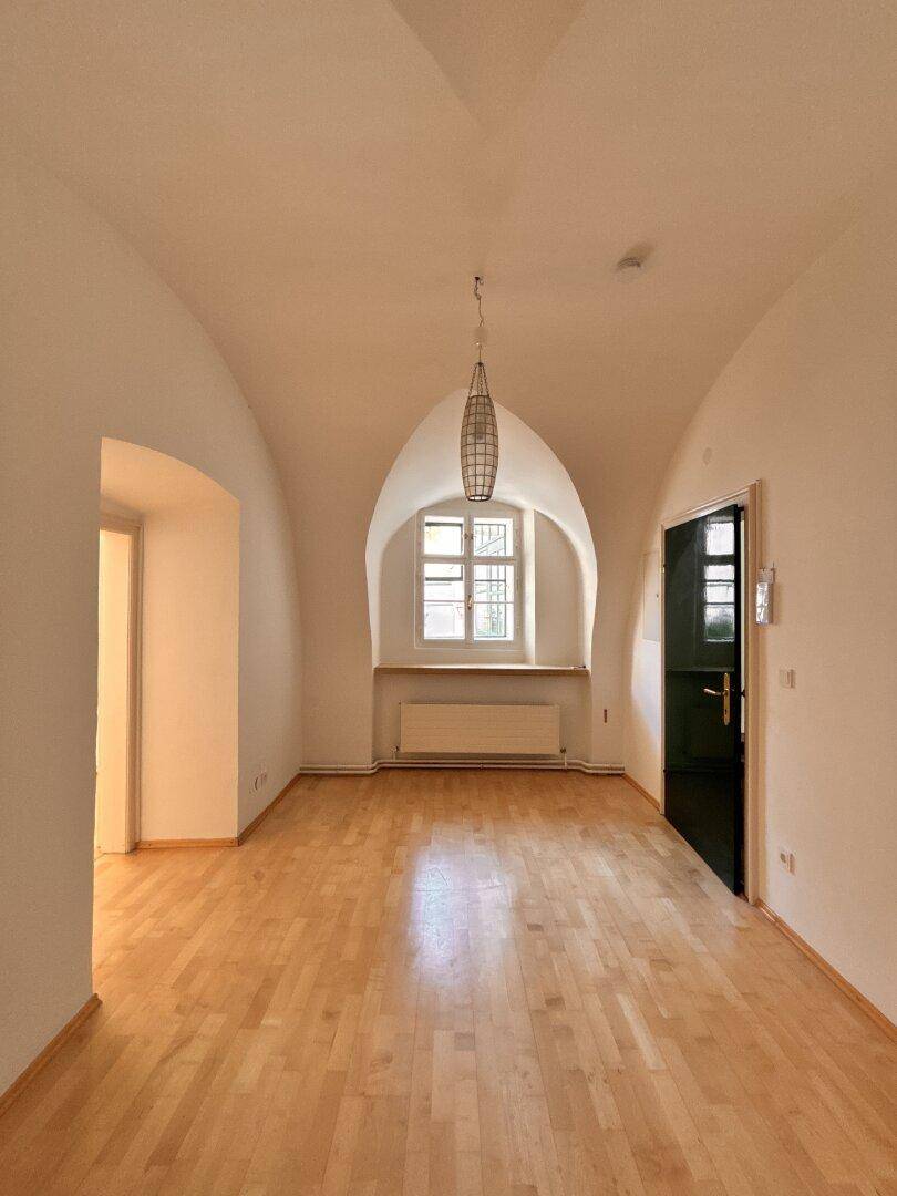Geräumiger, leerer Raum mit Holzboden, Gewölbedecke und einem Fenster in einer bogenförmigen Nische.