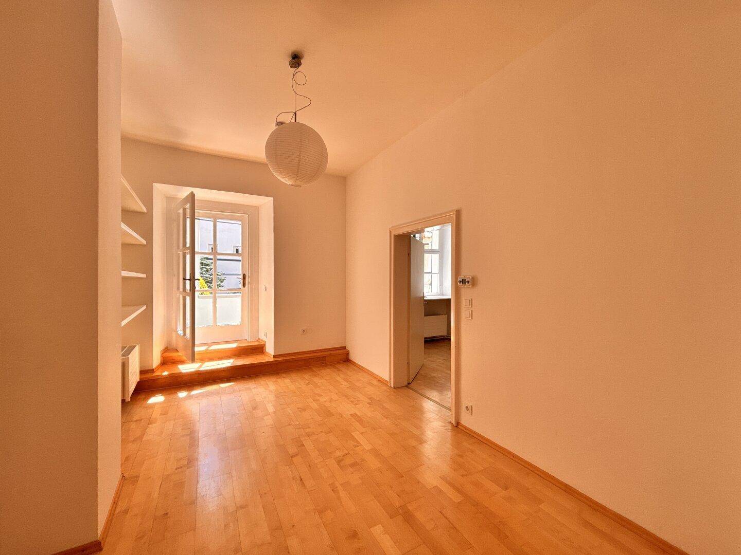 Heller, leerer Raum mit Holzboden und einer französischen Tür, die viel Tageslicht hereinlässt.