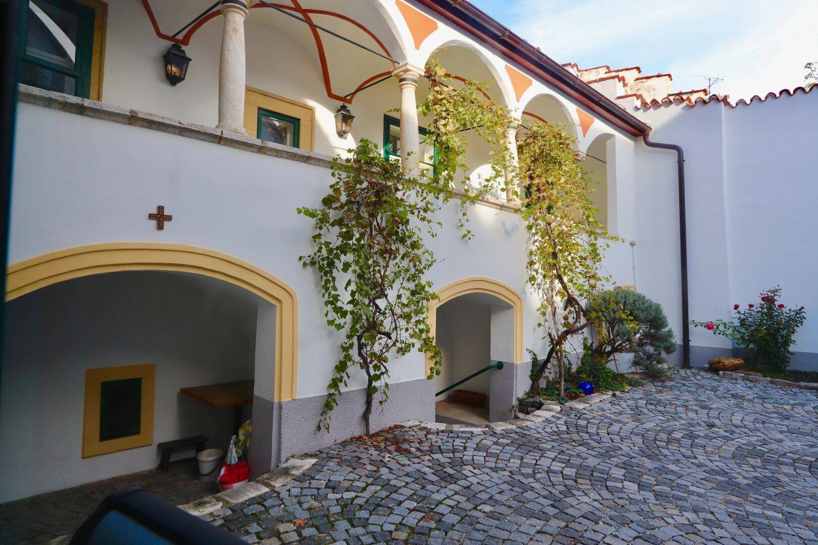 Gepflasterter Innenhof mit historischen Arkaden, Rankpflanzen und einem charmanten Altbau-Ambiente.