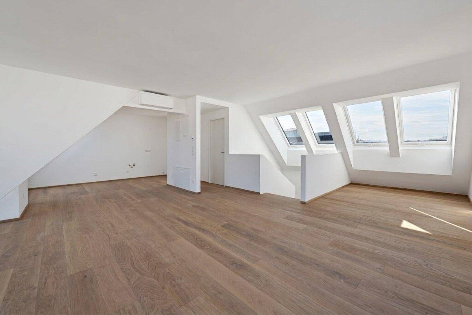 Heller Dachgeschossraum mit Holzboden, Klimaanlage und mehreren Dachfenstern für viel Tageslicht.