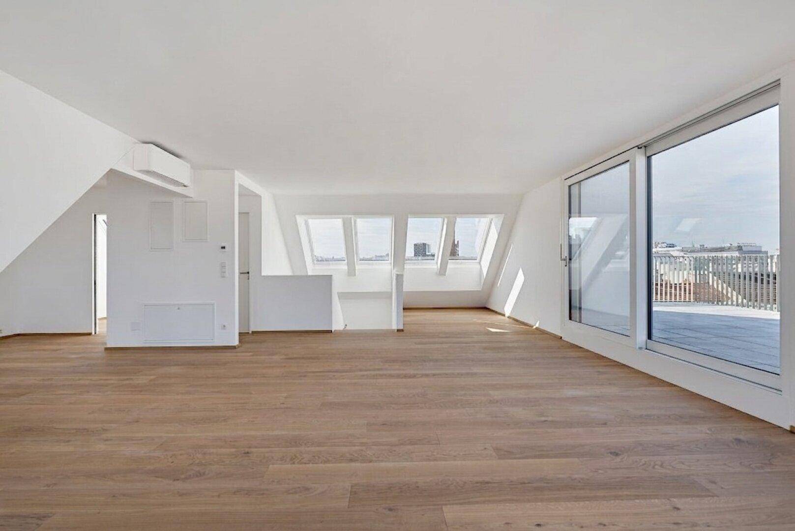 Geräumiger Dachgeschossraum mit Holzboden, Klimaanlage und Zugang zu einer Terrasse durch große Schiebetüren.