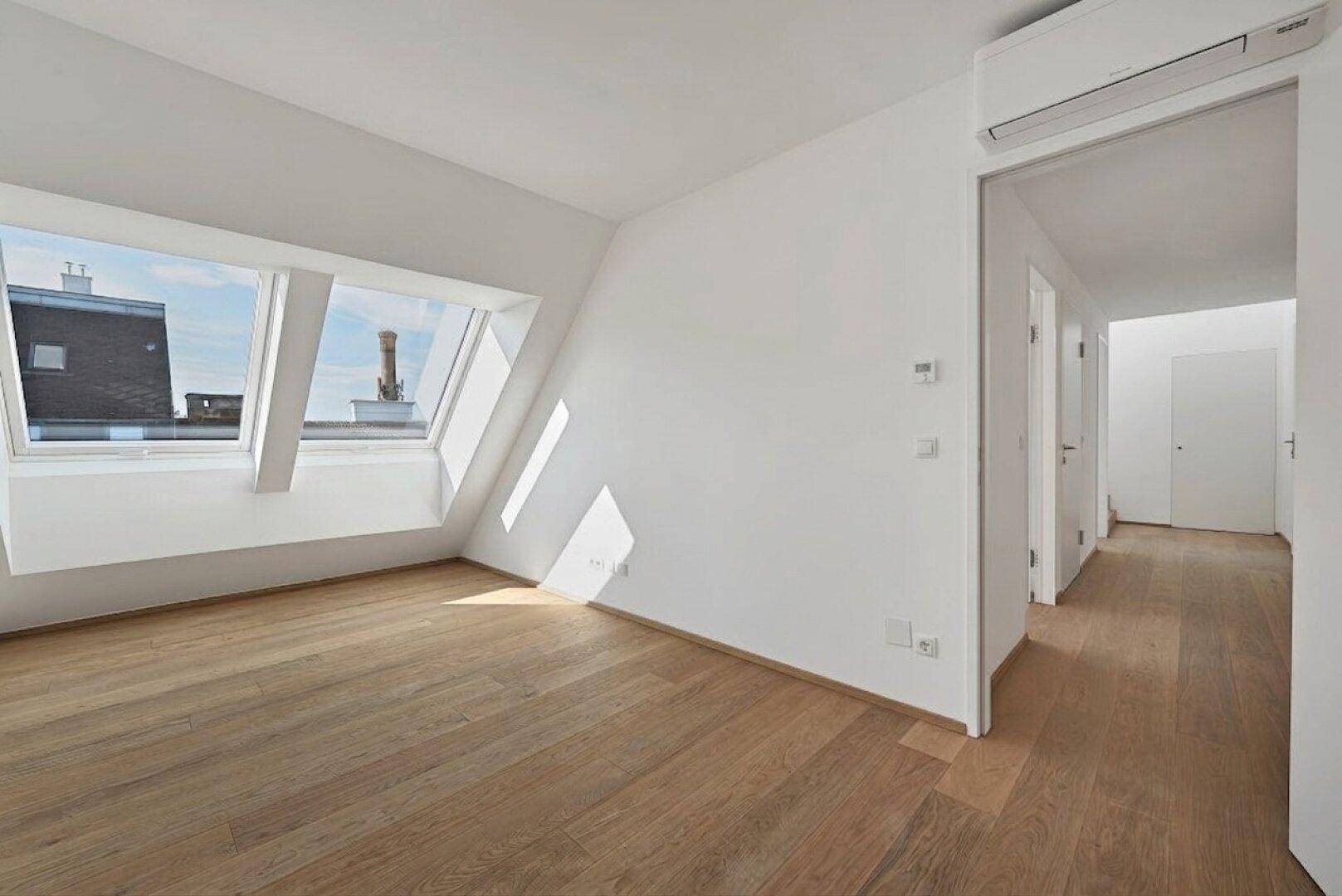 Heller Dachgeschossraum mit Holzboden, Klimaanlage und zwei Dachfenstern, die viel Licht spenden.