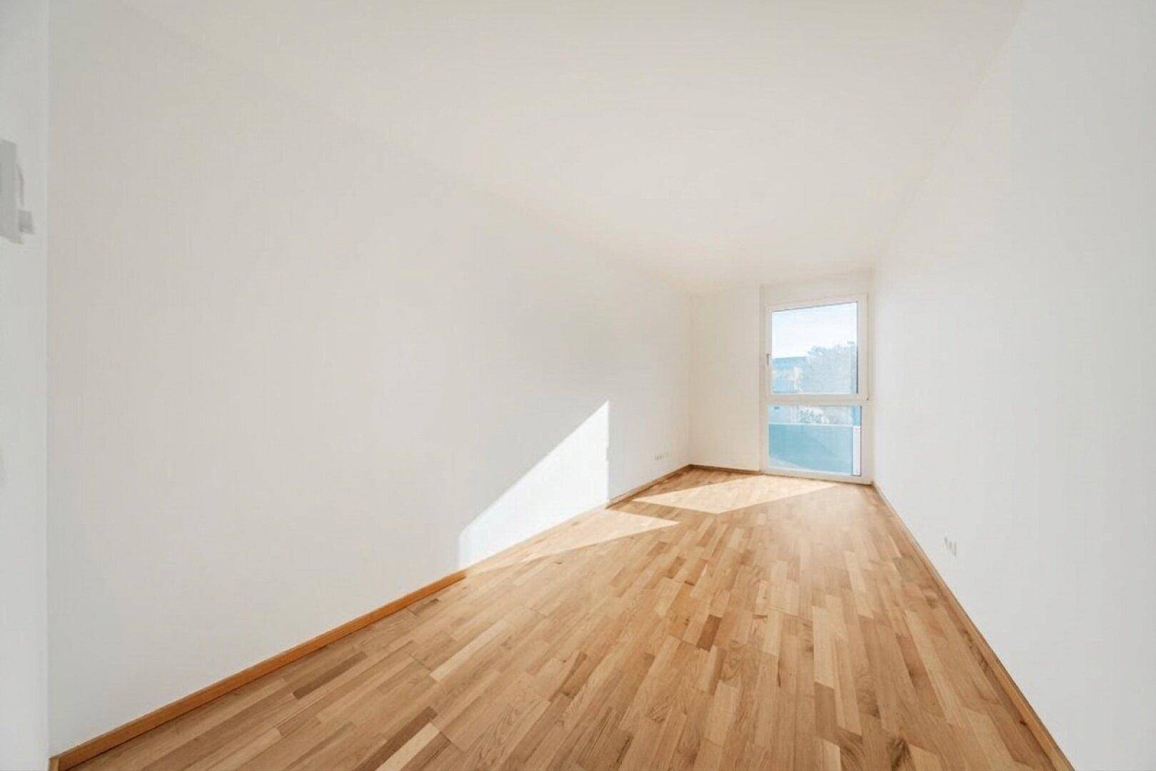 Heller, unmöblierter Raum mit Holzboden und großem Fenster.