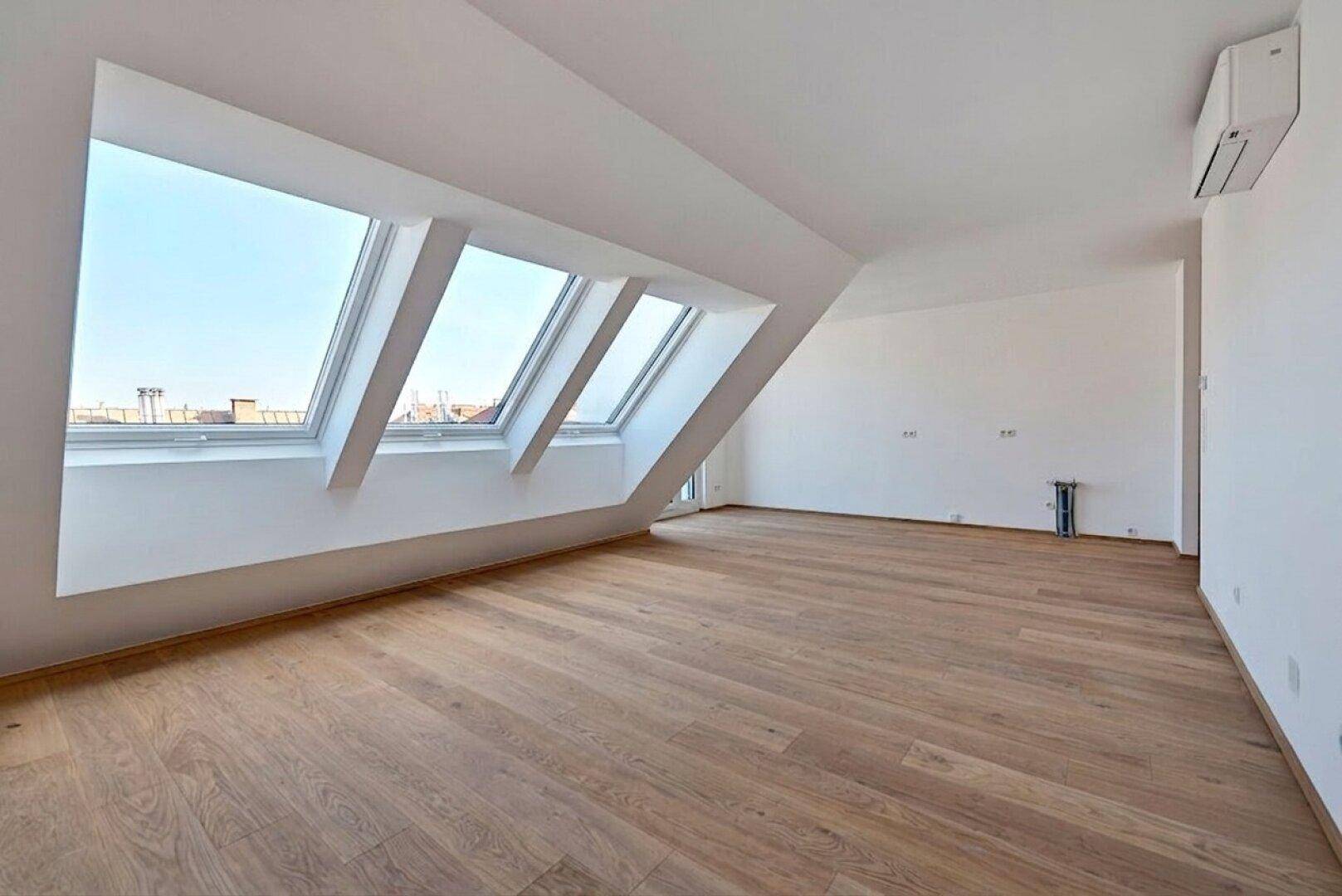 Heller, leerer Raum im Dachgeschoss mit Holzboden, Klimaanlage und drei schrägen Dachfenstern.