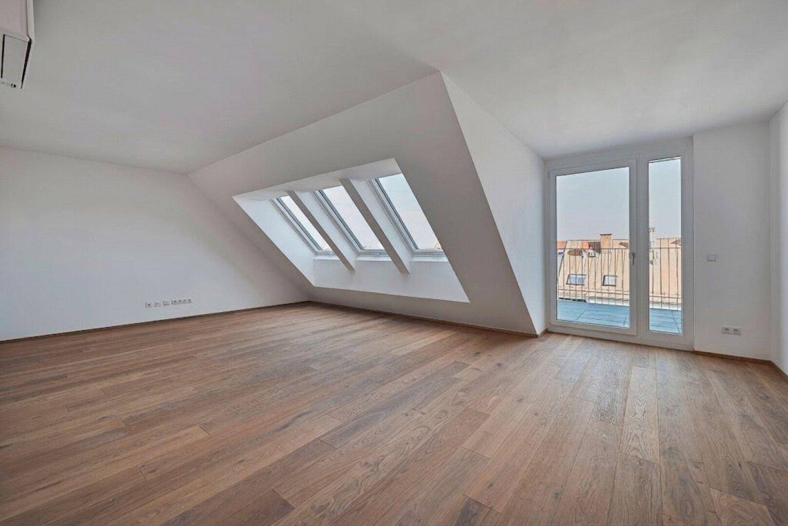 Leerer Dachgeschossraum mit Holzboden, Dachfenstern und Zugang zu einem Außenbereich.