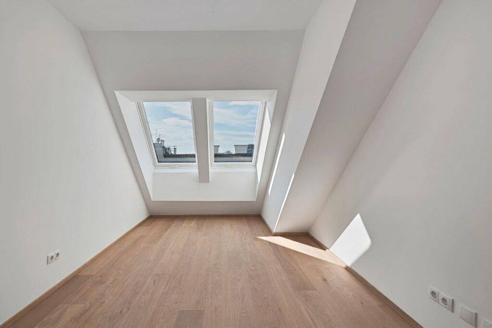Heller, leerer Raum im Dachgeschoss mit Holzboden und zwei großen Dachfenstern, die viel Licht hereinlassen.