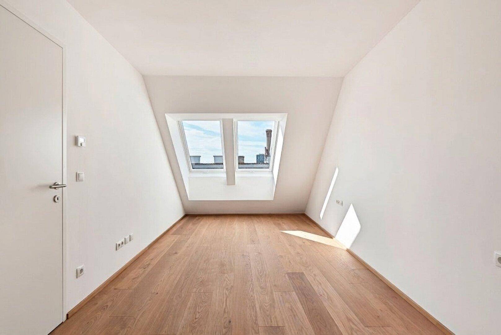 Leerer Raum im Dachgeschoss mit Holzboden und zwei Dachfenstern, ideal für Schlaf- oder Arbeitszimmer.