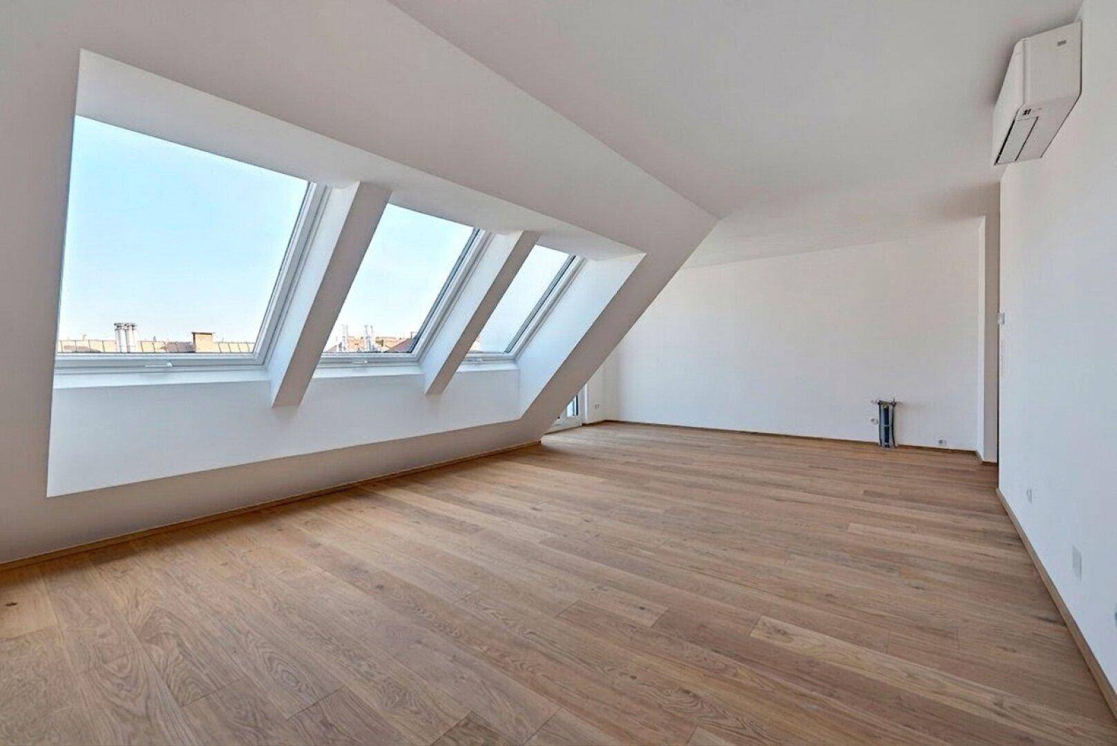 Helles Dachgeschosszimmer mit Holzboden und großen Dachfenstern, bietet viel natürliches Licht.