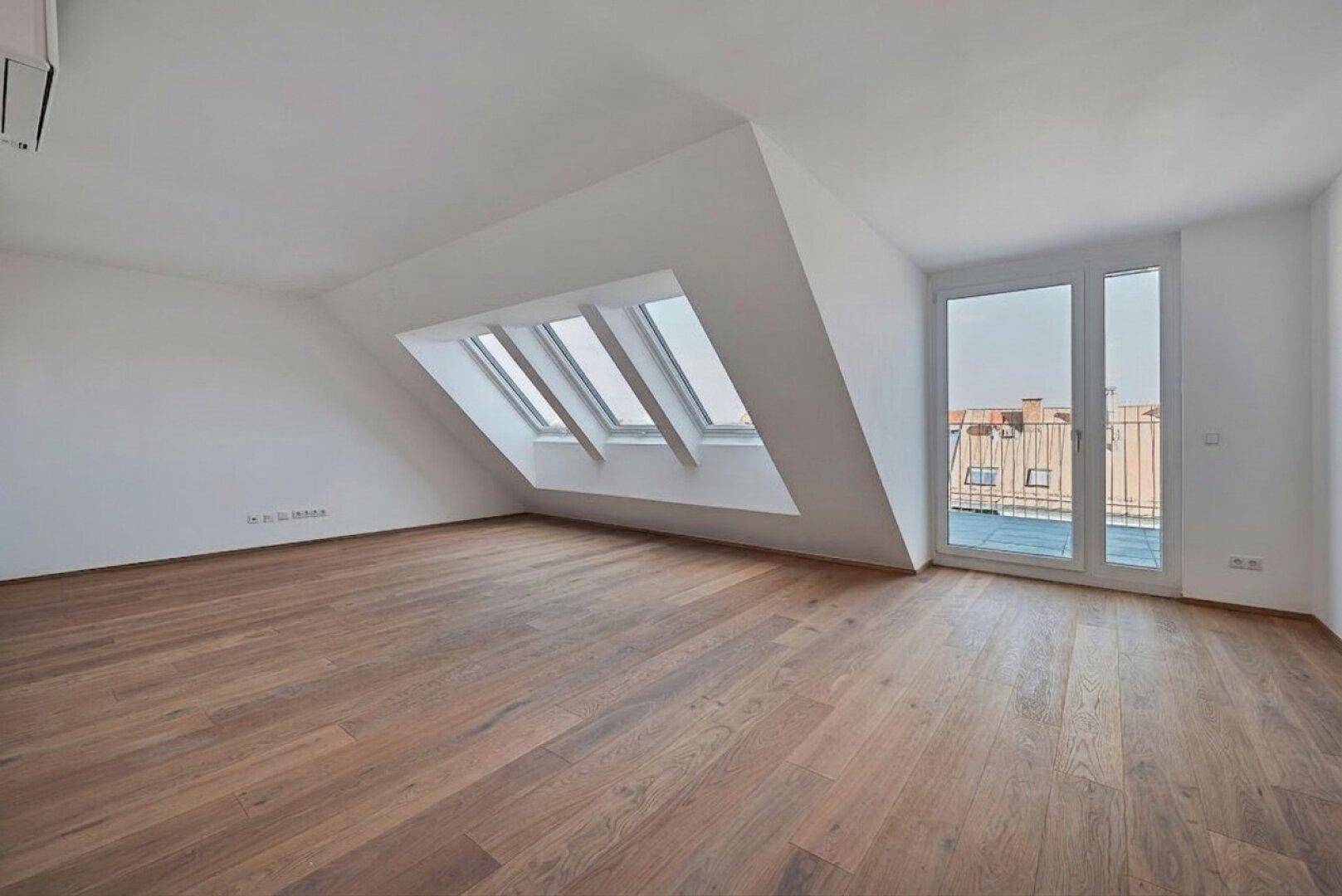 Lichtdurchfluteter Raum im Dachgeschoss mit Holzboden und Zugang zu einem Balkon.