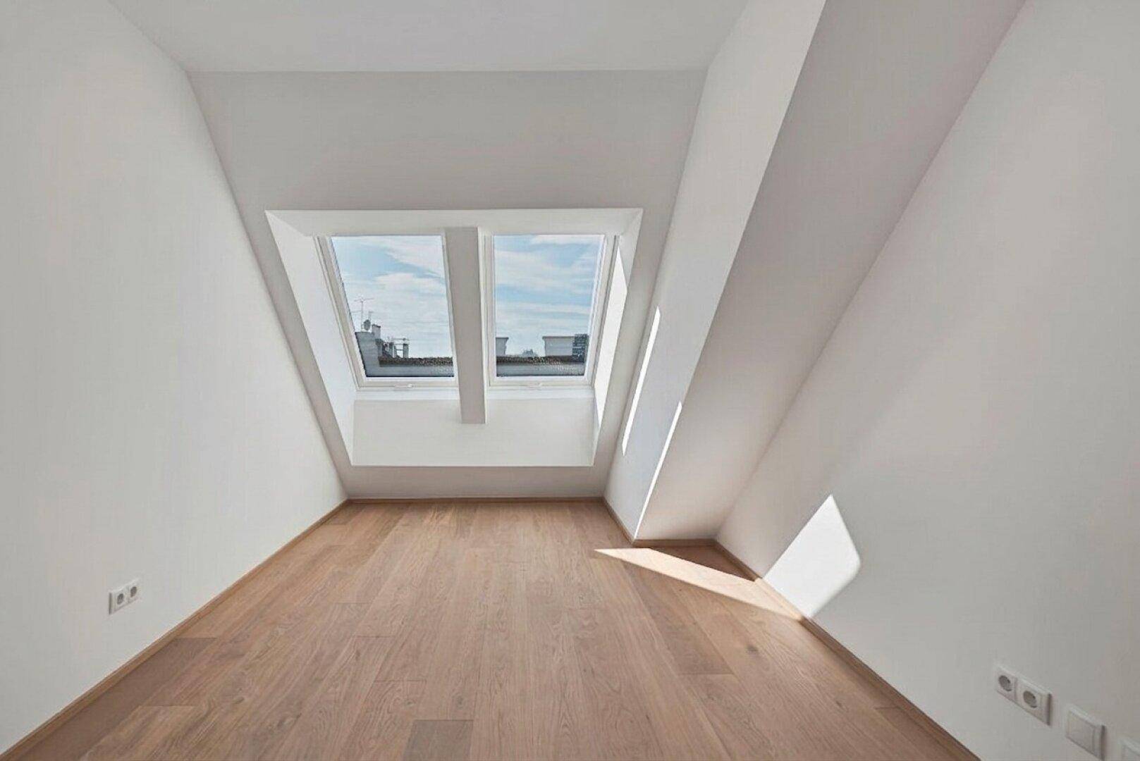 Helles Dachgeschosszimmer mit Holzboden und zwei großen Dachfenstern, unmöbliert.