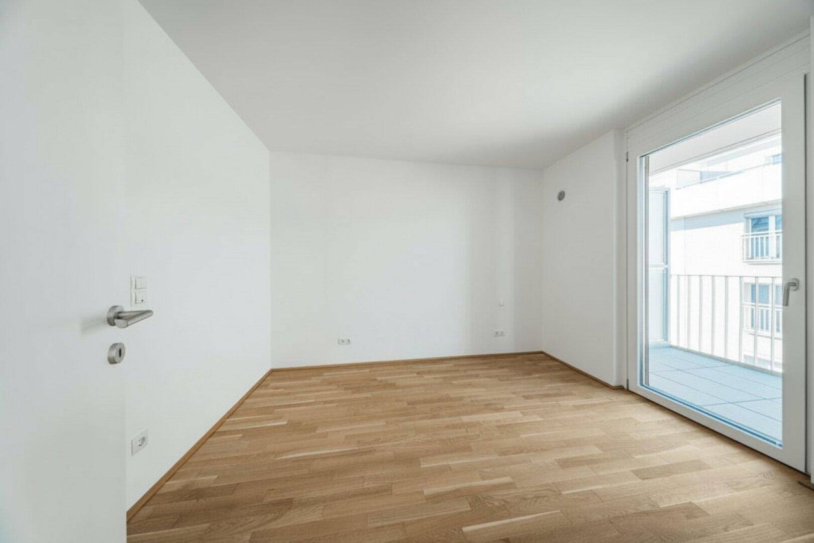 Heller, leerer Raum mit Parkettboden und Zugang zu einem französischen Balkon.
