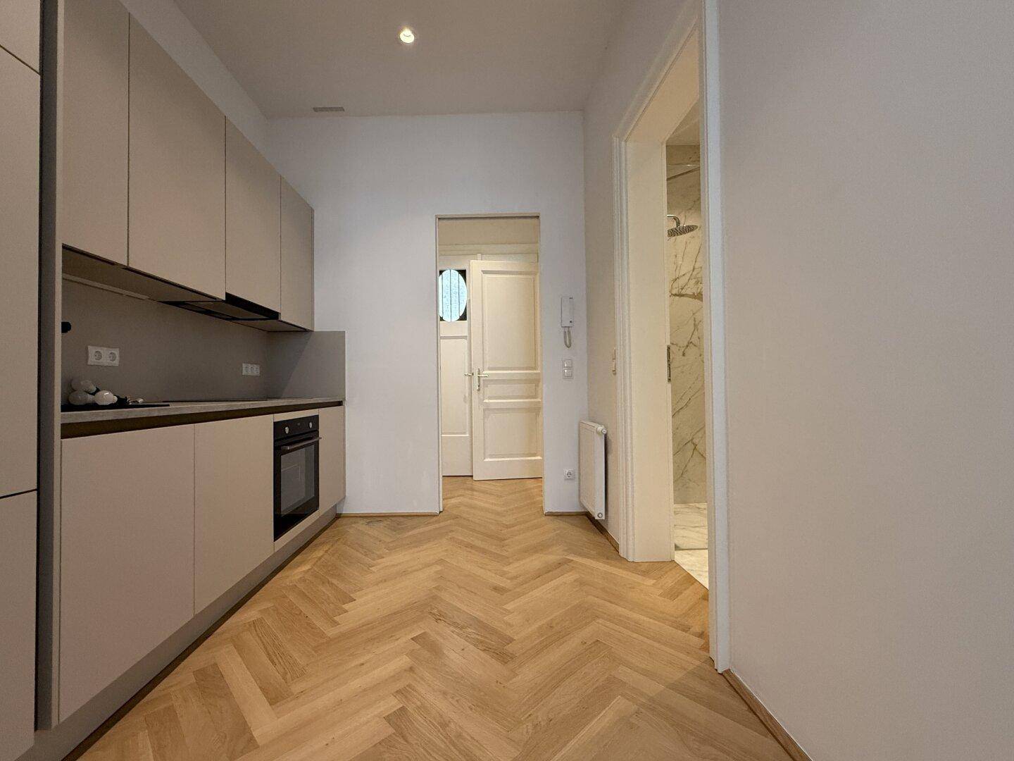 Moderne Küche mit hellgrauen Schränken, integriertem Backofen und Zugang zu Flur und Bad.