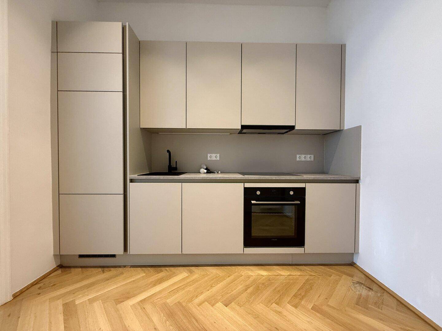 Voll ausgestattete moderne Küche mit hellgrauen Fronten, Backofen und integriertem Kühlschrank.
