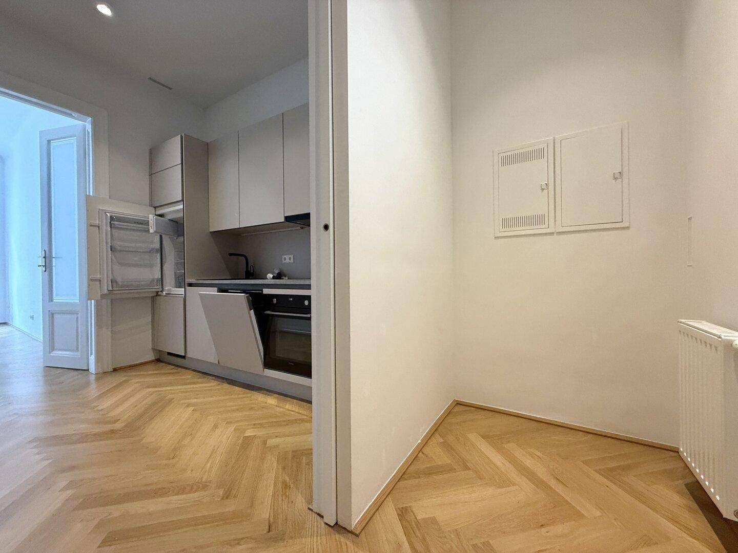 Funktionale Küche mit integriertem Kühlschrank und Blick in den angrenzenden Wohnbereich.