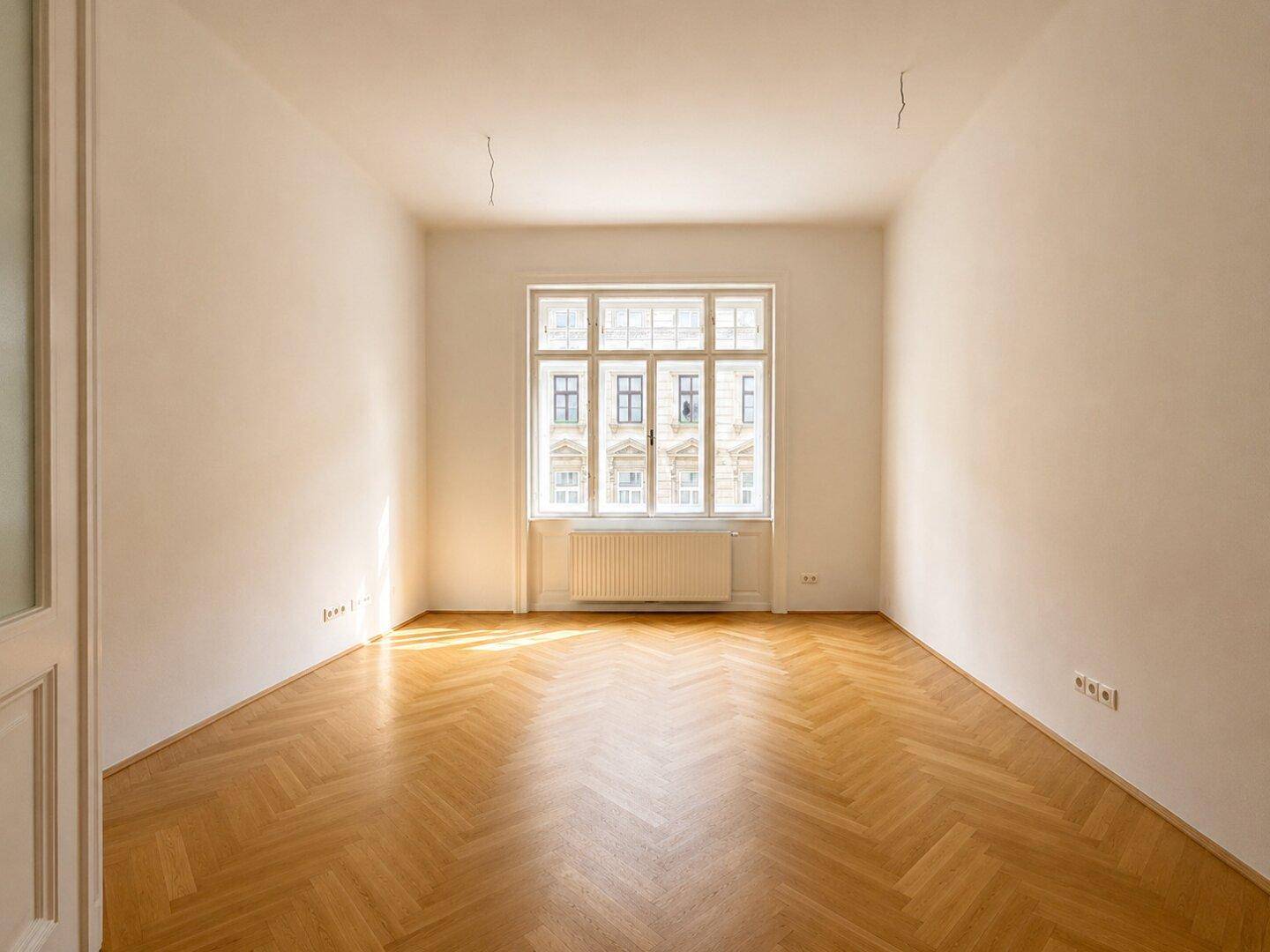 Geräumiges Zimmer mit klassischem Fischgrätparkett und großen Fenstern, bereit zur individuellen Gestaltung.