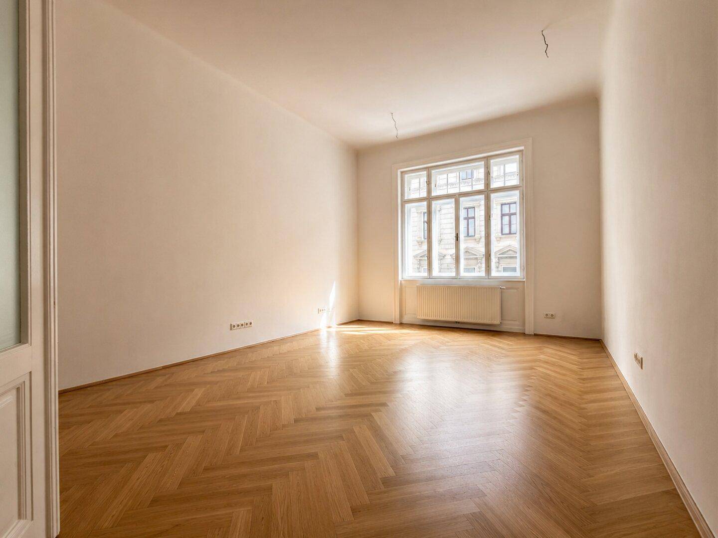 Lichtdurchflutetes Zimmer mit elegantem Fischgrätparkett und Blick auf die umliegenden Gebäude.