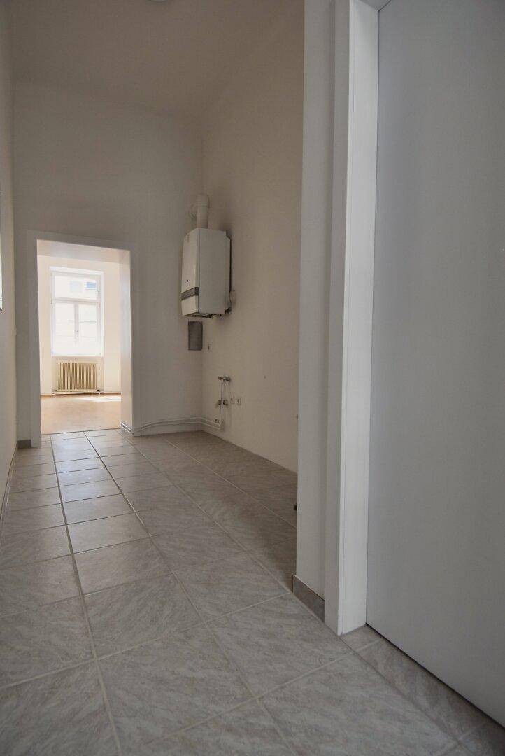 Flur mit Fliesenboden und an der Wand montiertem Warmwasserbereiter, führt zu einem weiteren Raum.