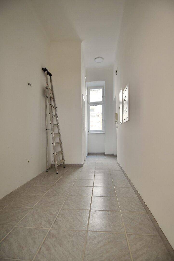 Langer, heller Flur mit Fliesenboden und einem Fenster am Ende, bietet viel natürliches Licht.