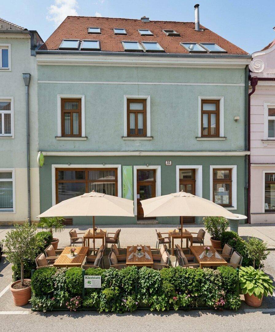 Historisches Gebäude mit einer charmanten Außenterrasse, ausgestattet mit Sonnenschirmen und Heckenbegrenzung.