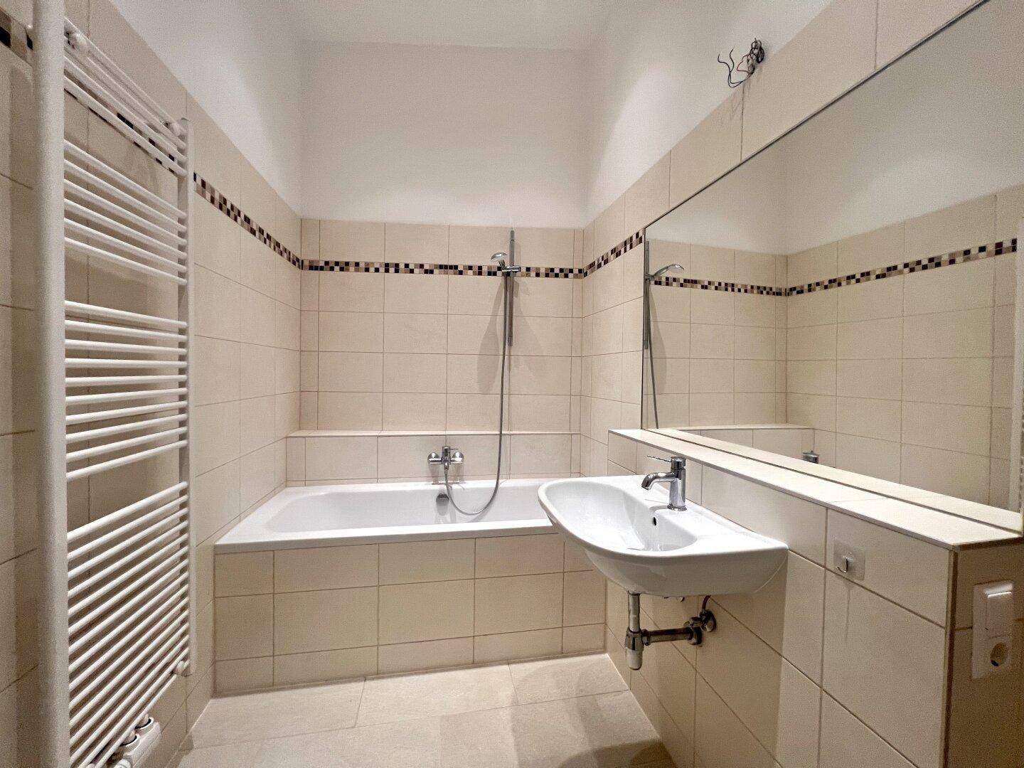 Helles Badezimmer mit Badewanne, Waschbecken, großem Spiegel und praktischem Handtuchheizkörper.