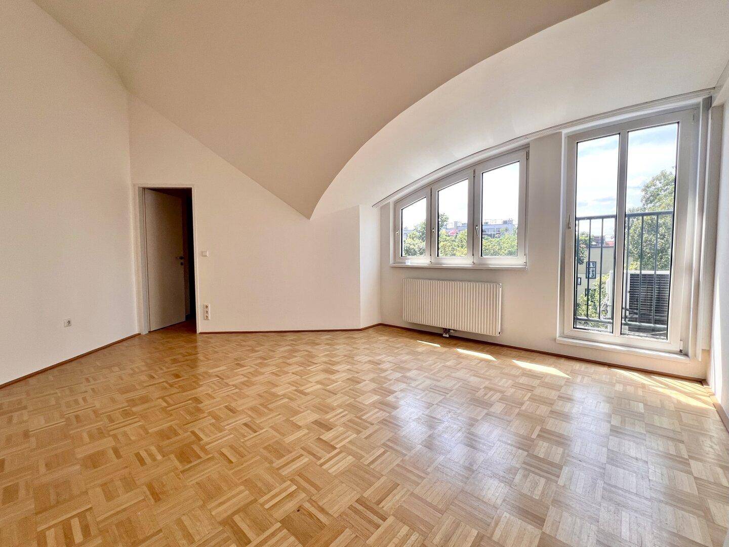 Geräumiges Zimmer im Dachgeschoss mit Parkettboden, schrägen Wänden und einem französischen Balkon für frische Luft.