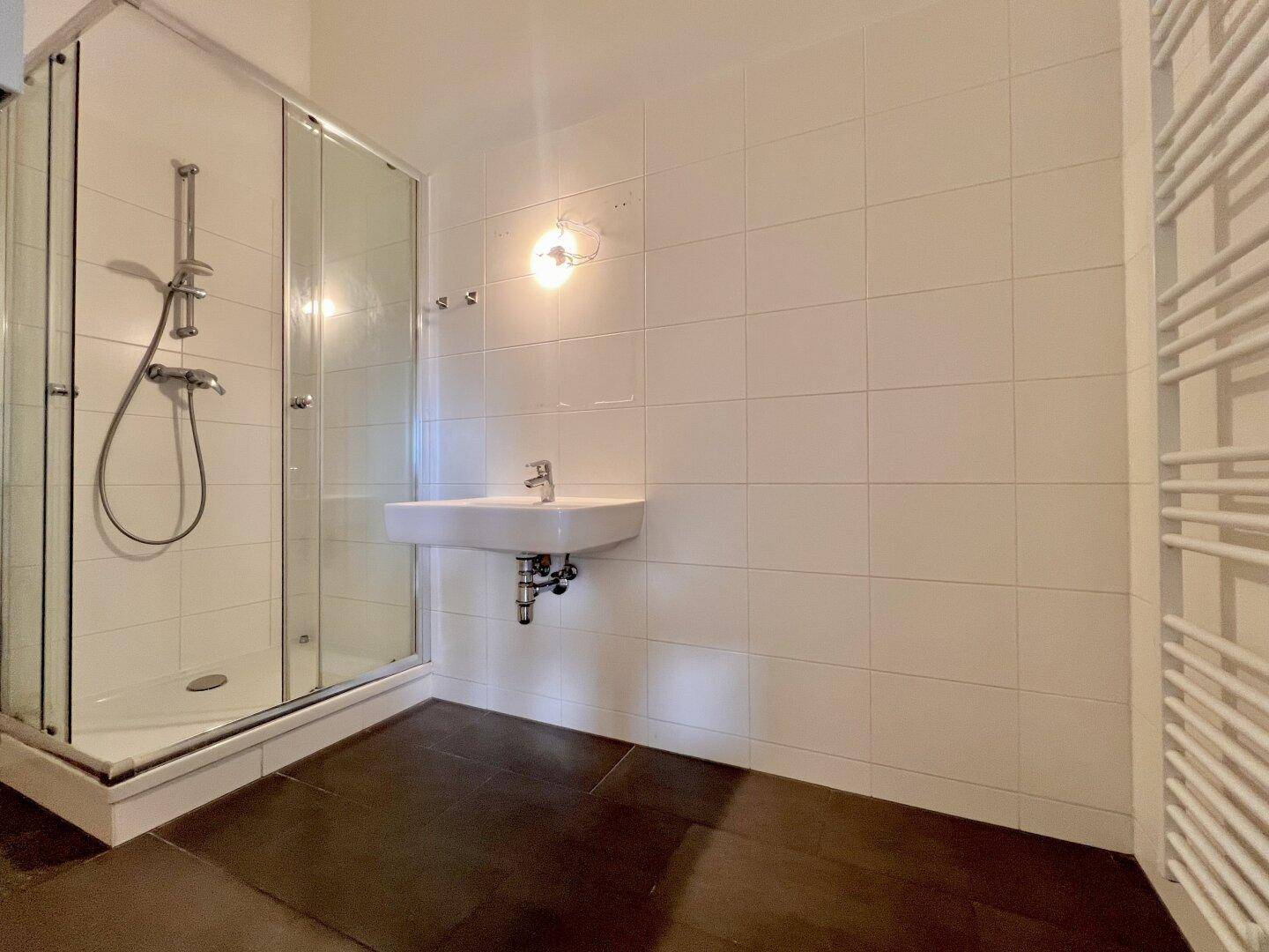 Modernes Badezimmer mit weiß gefliesten Wänden, Duschkabine, Einzelwaschbecken und beheiztem Handtuchhalter.