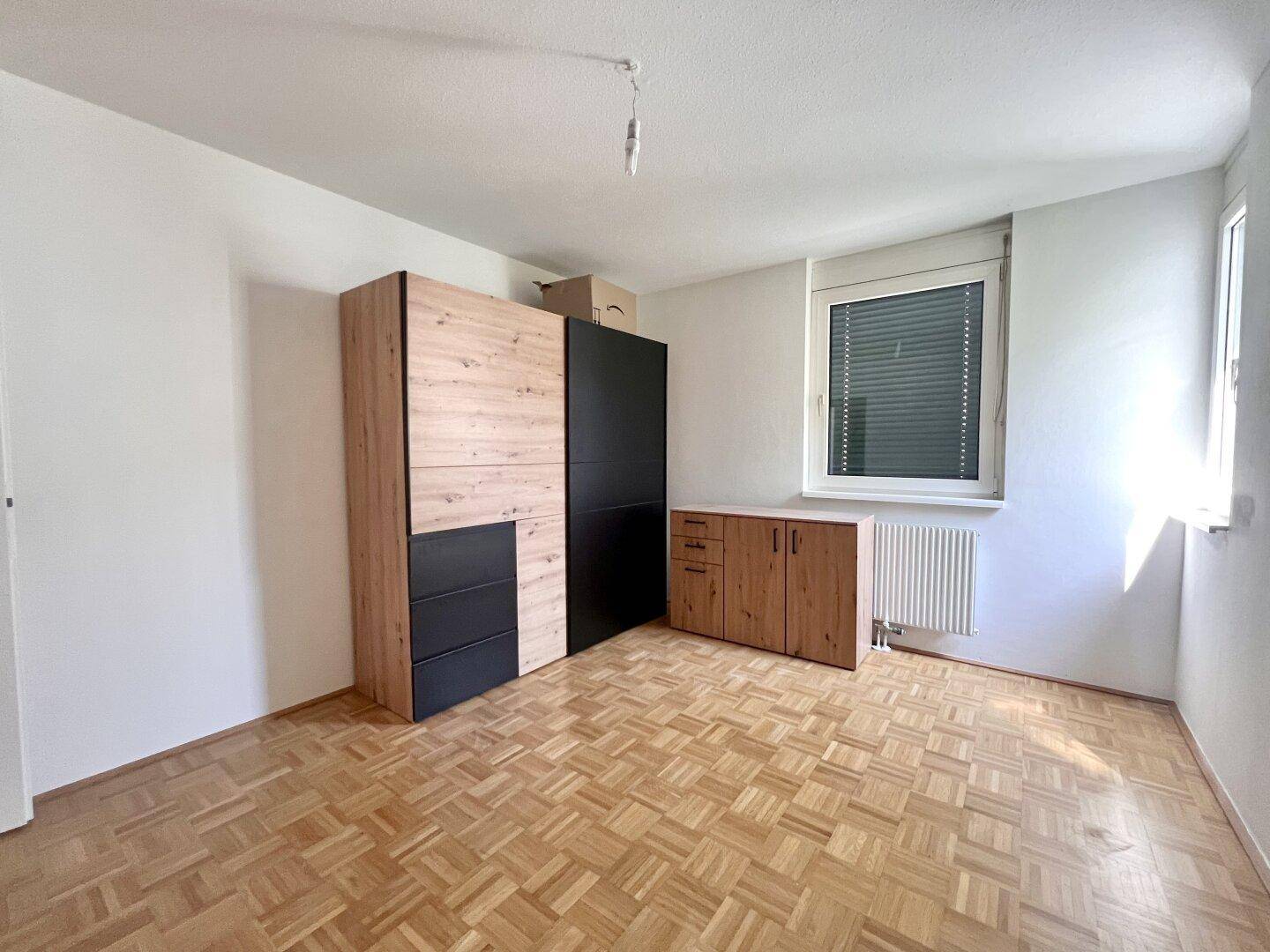 Schlafzimmer mit hellem Parkettboden, weißen Wänden und einem Fenster, ausgestattet mit zwei Kleiderschränken.