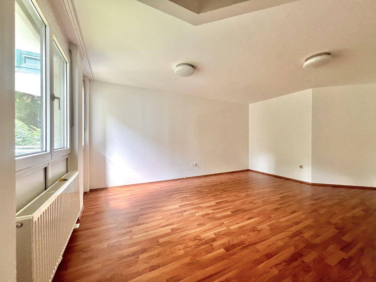 Leerer Wohnraum mit warmem Holzboden und hellen Wänden, bereit zur individuellen Gestaltung.