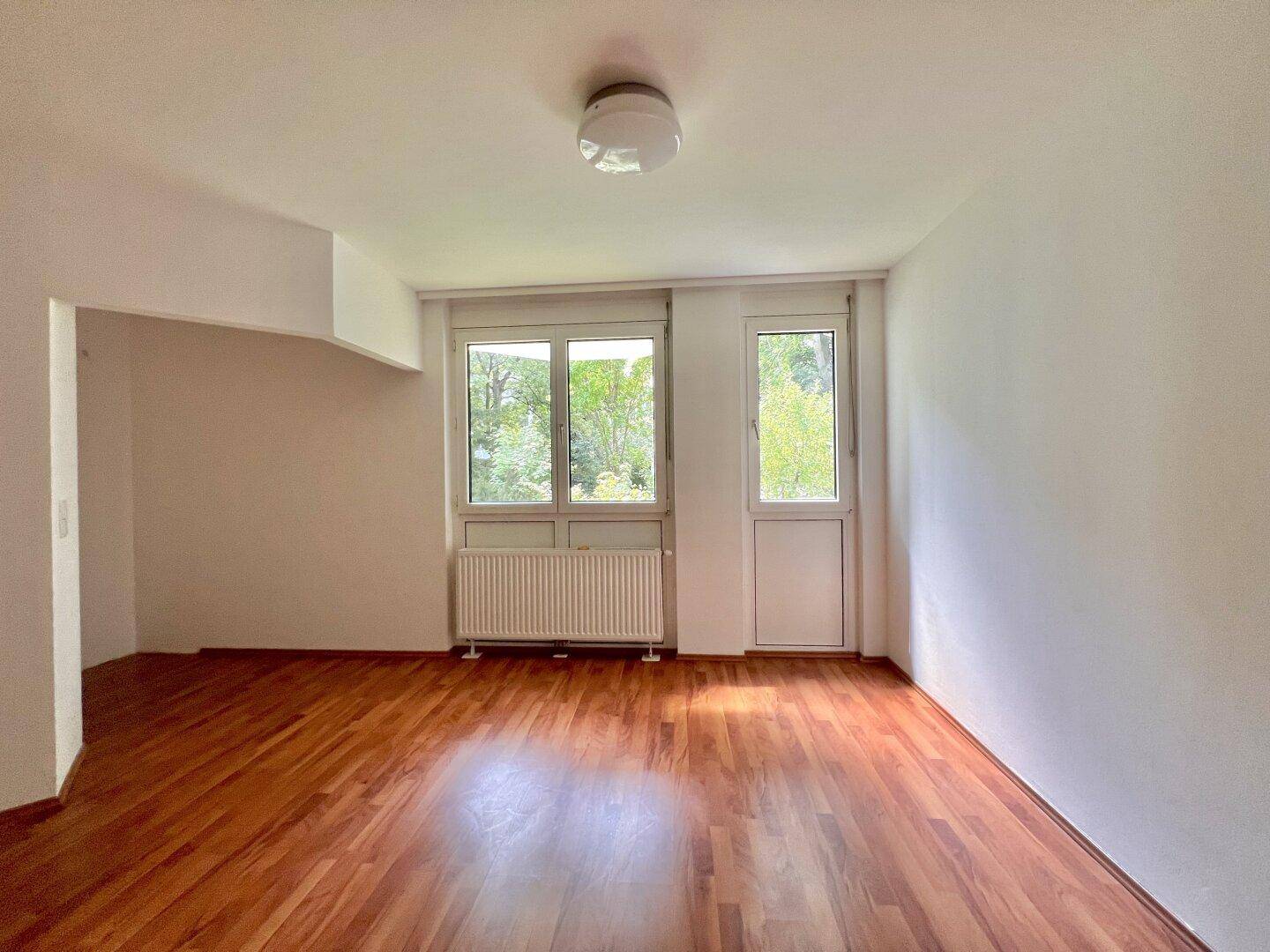Geräumiger, heller Raum mit Holzboden und großen Fenstern, die viel Tageslicht hereinlassen.