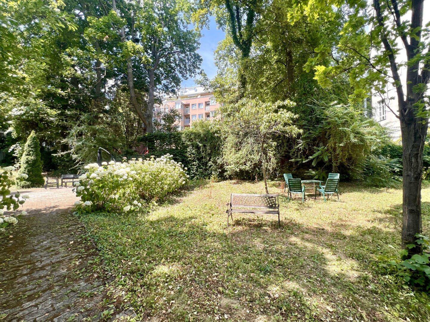 Gemeinschaftlicher Gartenbereich mit Sitzgelegenheiten, Bäumen und blühenden Sträuchern.