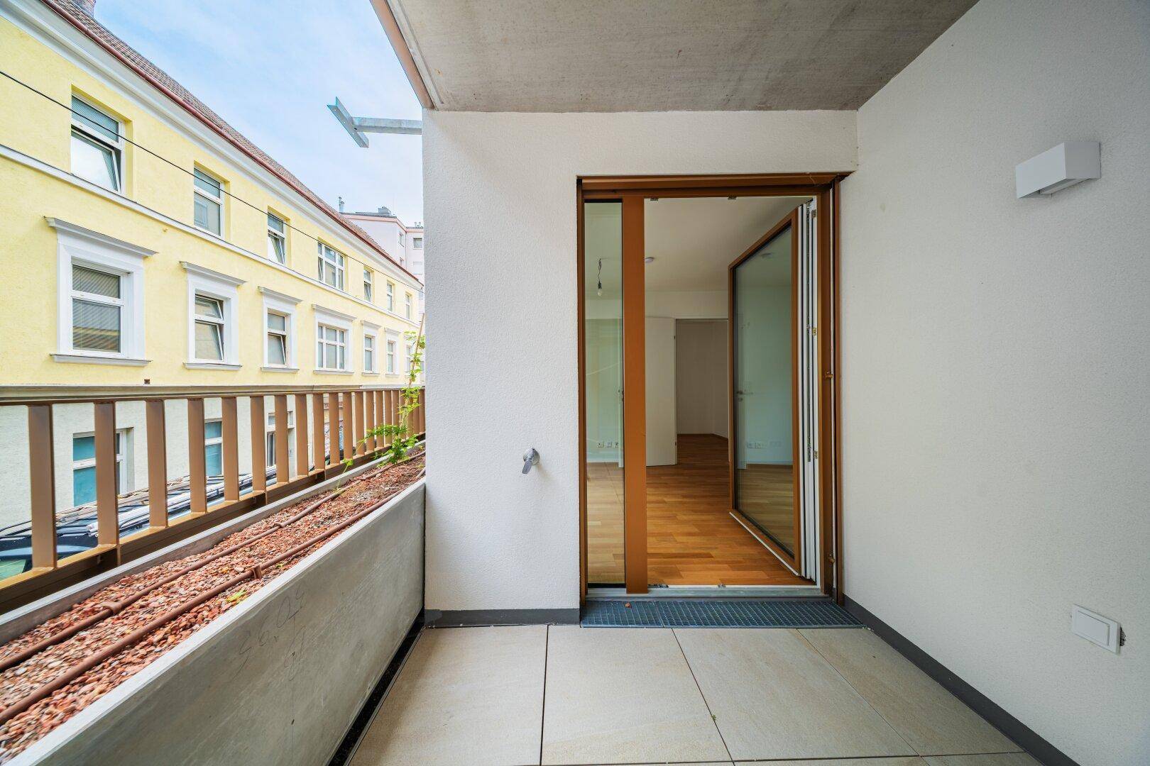 Heller Balkon mit Fliesenboden und Blick auf die umliegenden Gebäude der Stadt.