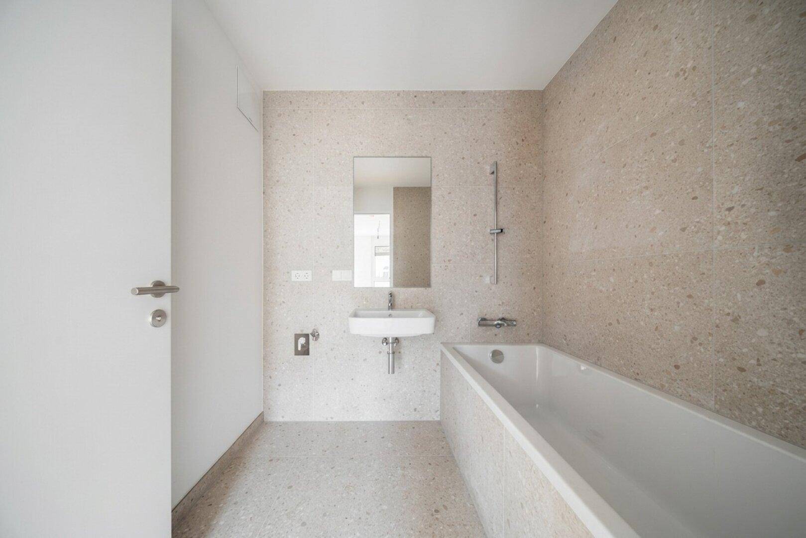 Modernes Badezimmer mit beigefarbenen Fliesen, Badewanne und kleinem Waschbecken.