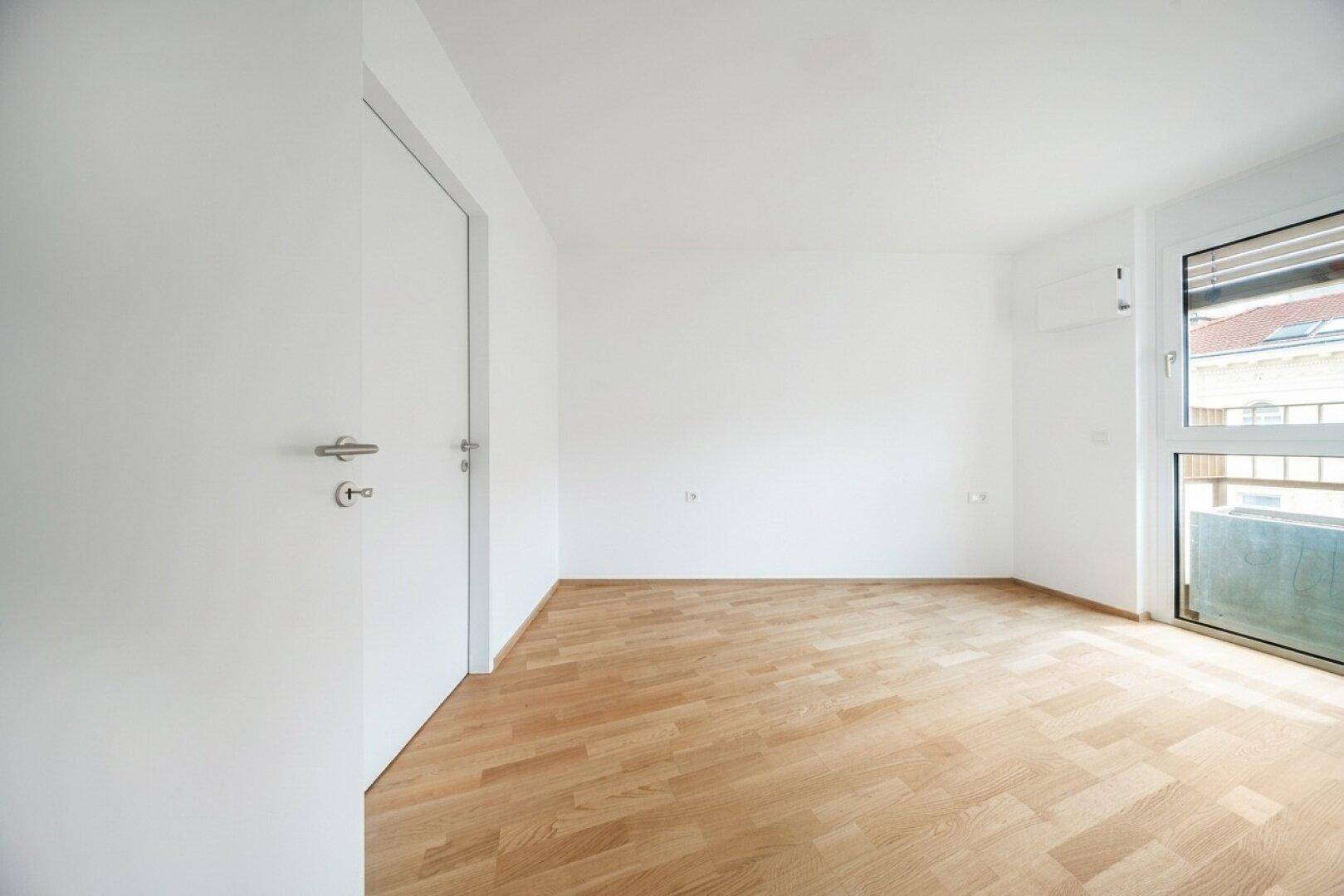 Leeres Zimmer mit Parkettboden, weiß gestrichenen Wänden und einem Fenster.