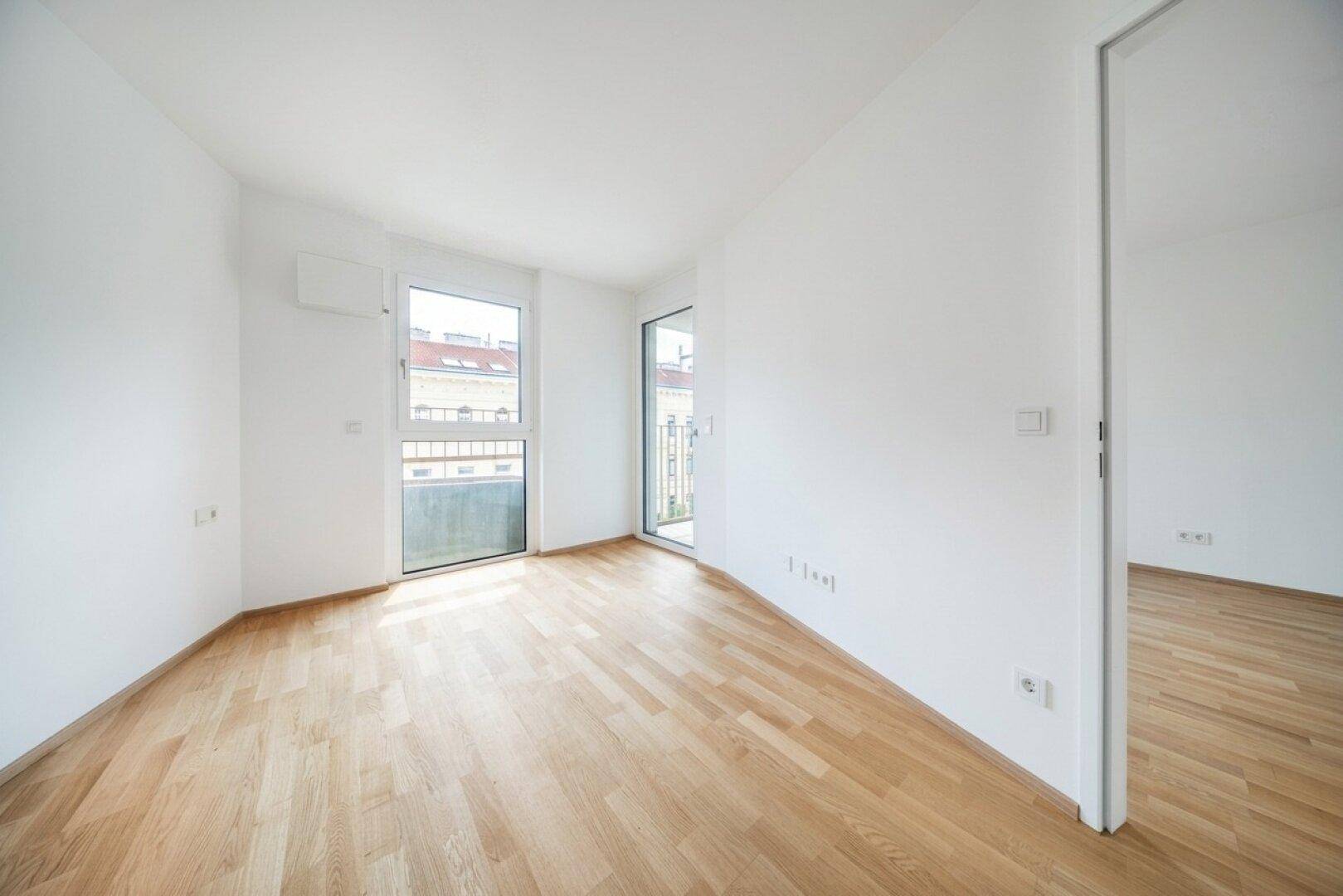 Lichtdurchfluteter Raum mit Holzboden und Fensterfront, die viel Tageslicht hereinlässt.