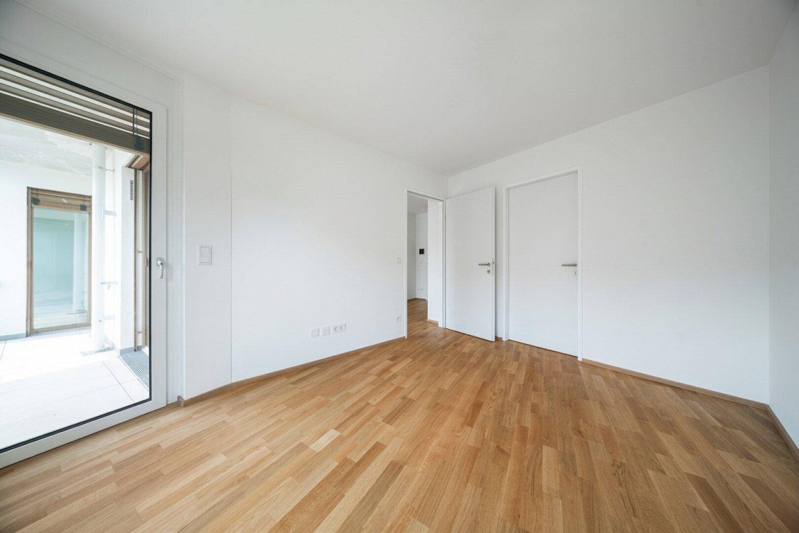 Geräumiges Zimmer mit Parkettboden und Zugang zu einem Außenbereich, ideal für individuelle Gestaltung.
