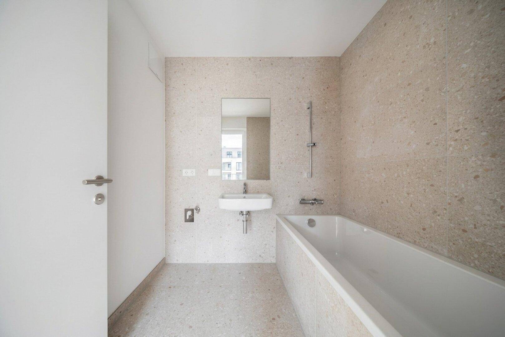 Modernes Badezimmer mit Badewanne, Einzelwaschbecken und hellen Fliesen an Wänden und Boden.