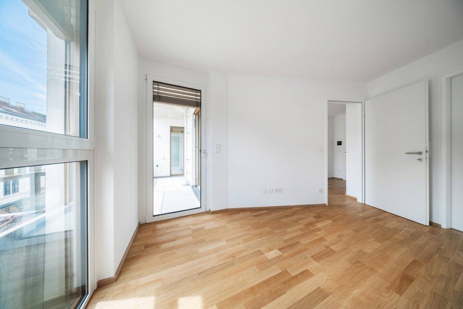 Geräumiges Zimmer mit Parkettboden und großen Fenstern, die den Raum mit Licht füllen.