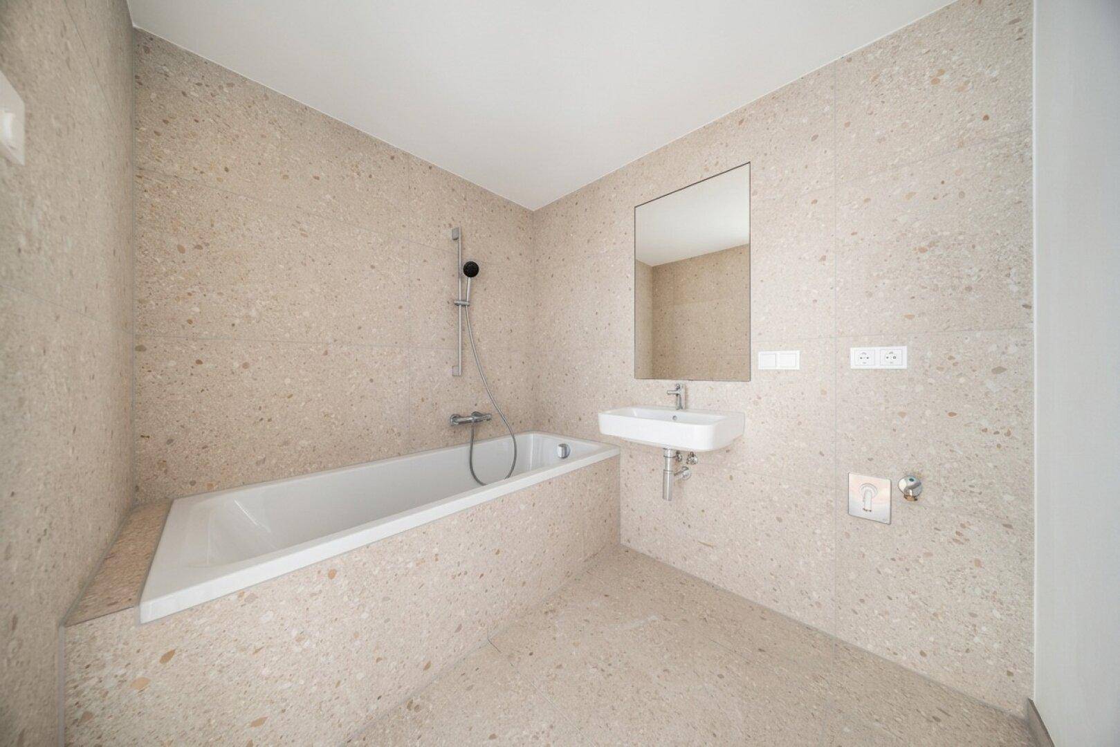 Modernes Badezimmer mit Badewanne, Einzelwaschbecken und hellen Fliesen an Wänden und Boden.